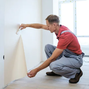 Vliestapetenkleister - Ein Tapezierer bringt Tapete an die Wand und streicht diese mit einem Werkzeug glatt, der Kleber kann sich gut verteilen.