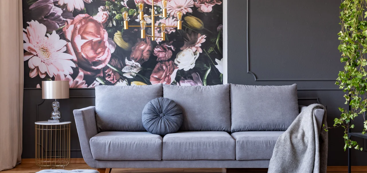 Fototapeten - Kissen und Decke auf einem stilvollen Sofa in einem grauen Wohnzimmer Interieur mit Efeu Pflanzen und Blumen an der Wand Tapete Fototapete Teppich Polsterstoffe