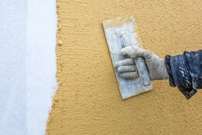 Fassaden-Arbeiten - Kelle mit Handschuh Hand verputzt eine Wand, Fassadenputz