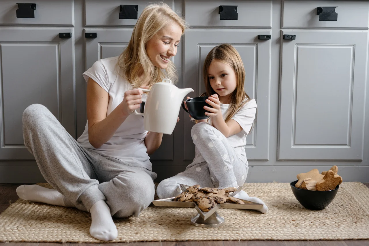 Mutter und Tochter genießen Tee und Kekse, sitzen in der Küche auf einem Teppichläufer. - Mutter und Tochter genießen Tee und Kekse, sitzen in der Küche auf einem Teppichläufer.